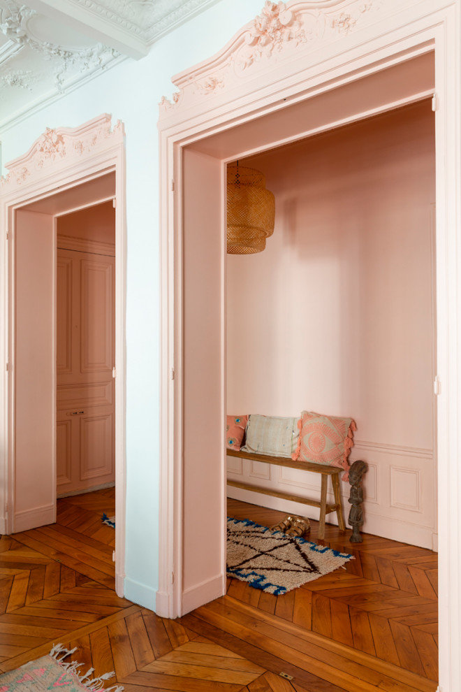Modern inredning av en mellanstor hall, med rosa väggar, mellanmörkt trägolv, en enkeldörr och brunt golv