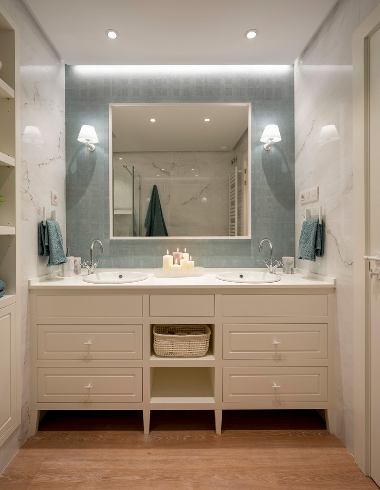 Photo of a mid-sized transitional master bathroom in Bilbao with beaded inset cabinets, white cabinets, an alcove shower, a wall-mount toilet, blue tile, white walls, laminate floors, a vessel sink, engineered quartz benchtops, brown floor, a hinged shower door and white benchtops.