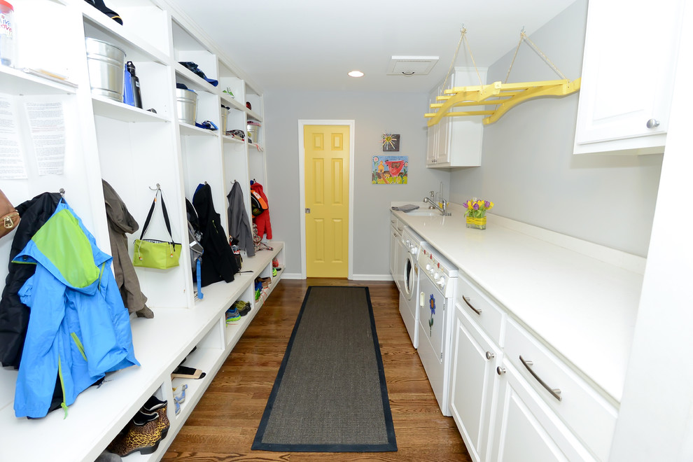 This is an example of a traditional galley utility room in Kansas City with an undermount sink, raised-panel cabinets, white cabinets, grey walls, medium hardwood floors and a side-by-side washer and dryer.