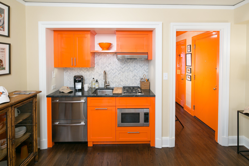 This is an example of a small transitional single-wall eat-in kitchen in Philadelphia with a single-bowl sink, dark hardwood floors, brown floor, flat-panel cabinets, orange cabinets, granite benchtops, grey splashback, stone tile splashback and stainless steel appliances.