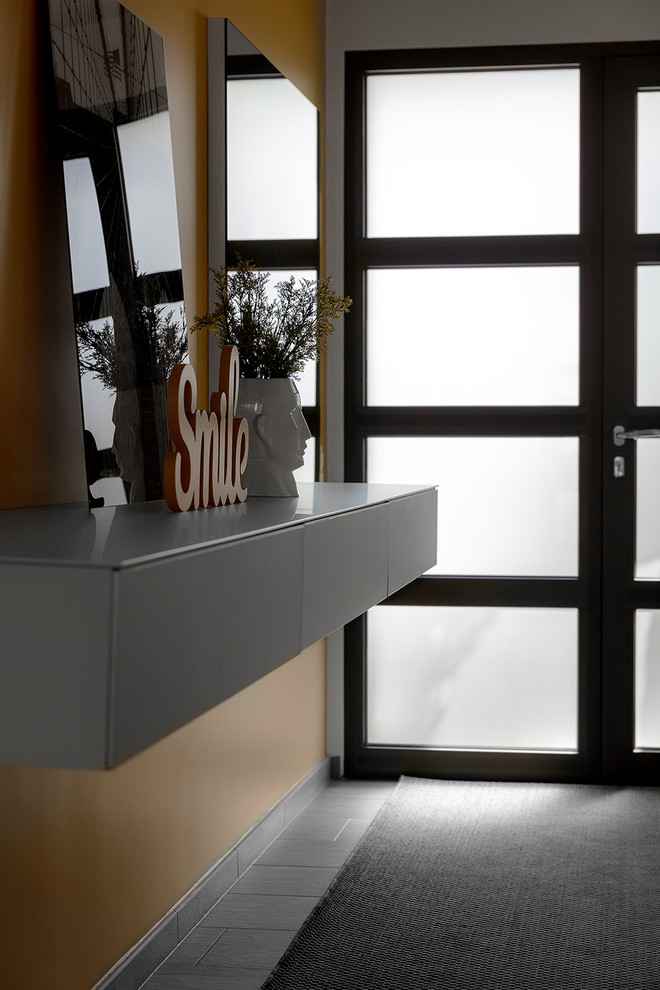 Example of a mid-sized trendy ceramic tile and gray floor foyer design with yellow walls and a black front door