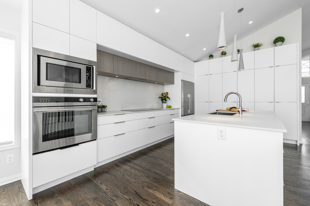 Photo of a mid-sized contemporary u-shaped eat-in kitchen in Ottawa with an undermount sink, flat-panel cabinets, white cabinets, stainless steel appliances, with island, brown floor, quartz benchtops, white splashback, porcelain splashback, dark hardwood floors and grey benchtop.