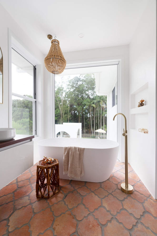 Стильный дизайн: главная ванная комната в средиземноморском стиле с плоскими фасадами, белыми фасадами, отдельно стоящей ванной, открытым душем, белой плиткой, белыми стенами, полом из терракотовой плитки, настольной раковиной, столешницей из дерева, оранжевым полом, открытым душем, коричневой столешницей, тумбой под одну раковину и подвесной тумбой - последний тренд