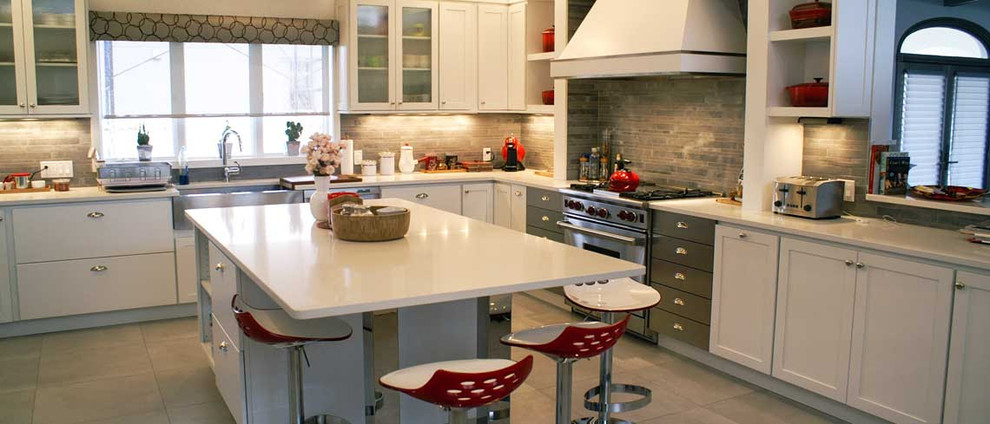 Enclosed kitchen - large transitional l-shaped enclosed kitchen idea with a farmhouse sink, shaker cabinets, white cabinets, quartzite countertops, gray backsplash, stone tile backsplash, stainless steel appliances and an island