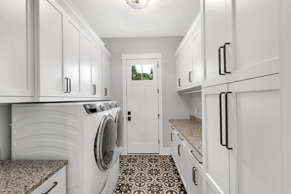 Foto på en mellanstor lantlig beige parallell tvättstuga enbart för tvätt, med skåp i shakerstil, vita skåp, granitbänkskiva, grå väggar, klinkergolv i keramik, en tvättmaskin och torktumlare bredvid varandra och flerfärgat golv