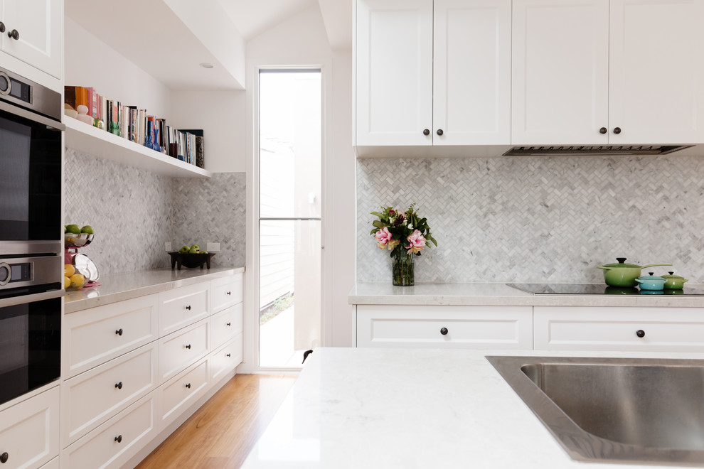 Mid-sized transitional u-shaped light wood floor and brown floor eat-in kitchen photo in DC Metro with an undermount sink, recessed-panel cabinets, white cabinets, quartz countertops, white backsplash, marble backsplash, stainless steel appliances, a peninsula and white countertops