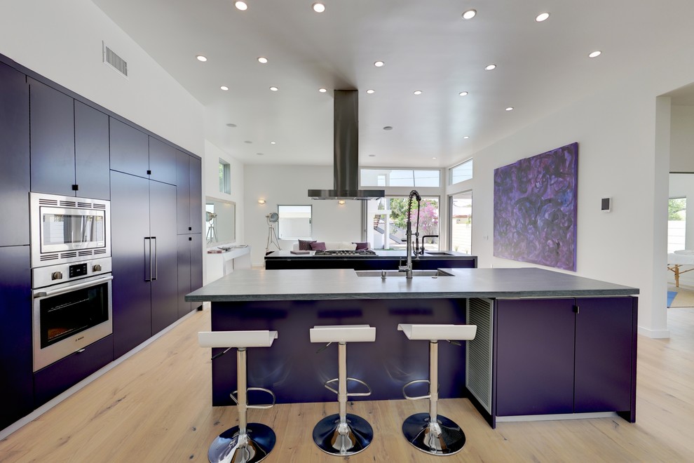 This is an example of a mid-sized contemporary l-shaped separate kitchen in Los Angeles with a farmhouse sink, flat-panel cabinets, purple cabinets, stainless steel appliances, light hardwood floors, multiple islands and beige floor.