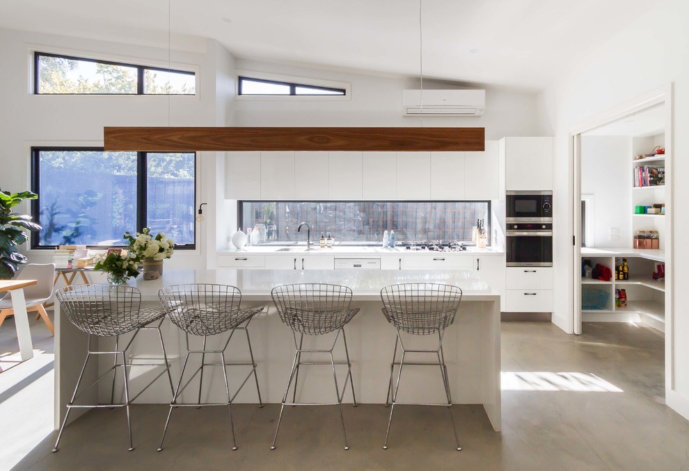 Design ideas for a large contemporary galley open plan kitchen in Melbourne with a double-bowl sink, flat-panel cabinets, white cabinets, quartz benchtops, window splashback, stainless steel appliances, concrete floors and with island.