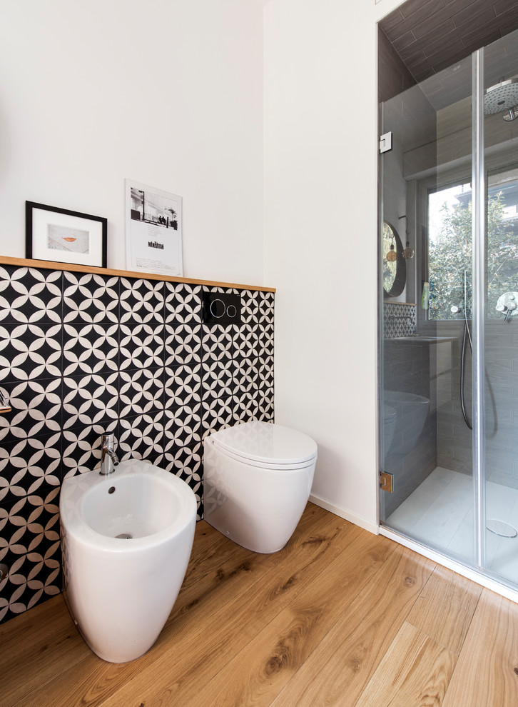 Photo of a mid-sized scandinavian master bathroom in Milan with flat-panel cabinets, light wood cabinets, an alcove shower, a two-piece toilet, black and white tile, terra-cotta tile, white walls, concrete floors, an integrated sink, solid surface benchtops, grey floor, a hinged shower door and white benchtops.
