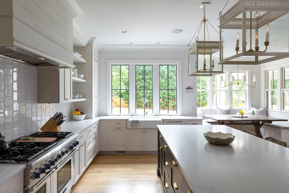 Inspiration for a country l-shaped eat-in kitchen in Charlotte with a farmhouse sink, shaker cabinets, white cabinets, white splashback, stainless steel appliances, light hardwood floors, with island, beige floor and white benchtop.