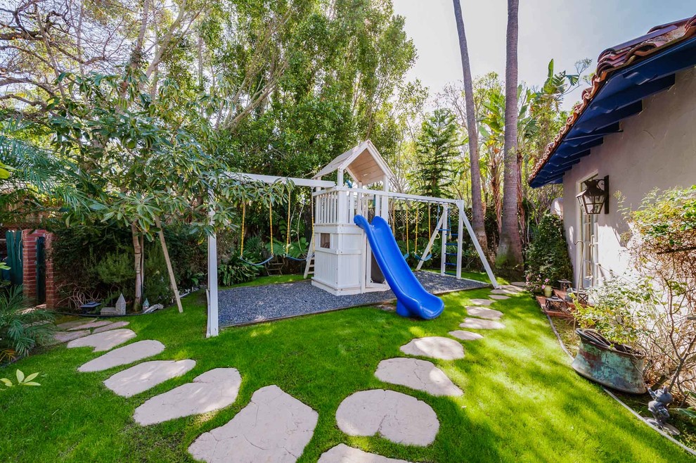 Large mediterranean backyard partial sun garden in Los Angeles with with outdoor playset and natural stone pavers.