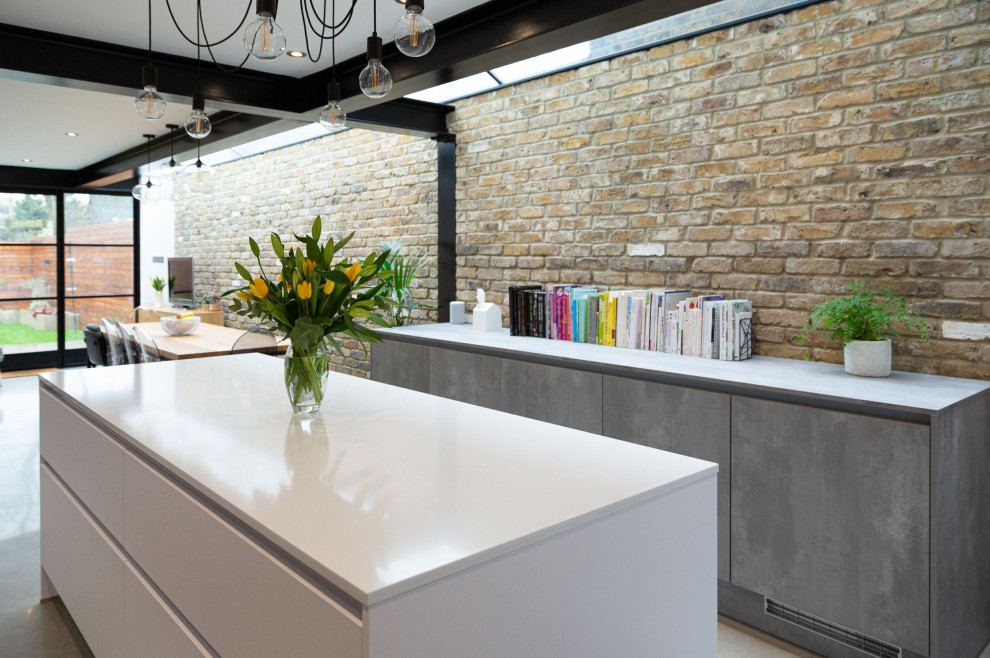 Photo of a large contemporary galley open plan kitchen in London with an undermount sink, flat-panel cabinets, white cabinets, solid surface benchtops, grey splashback, porcelain splashback, black appliances, concrete floors, with island, grey floor and white benchtop.