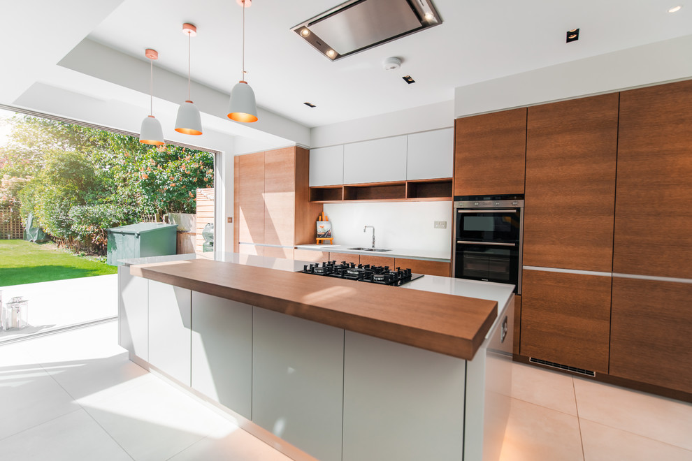 This is an example of a mid-sized contemporary galley eat-in kitchen in London with a single-bowl sink, flat-panel cabinets, medium wood cabinets, quartzite benchtops, white splashback, stainless steel appliances, with island, white benchtop and white floor.