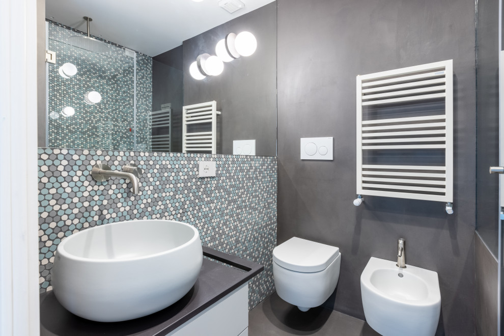 Inredning av ett modernt litet svart svart badrum, med en dusch i en alkov, en toalettstol med separat cisternkåpa, grå kakel, mosaik, grå väggar, betonggolv, ett fristående handfat, bänkskiva i akrylsten, grått golv och dusch med gångjärnsdörr