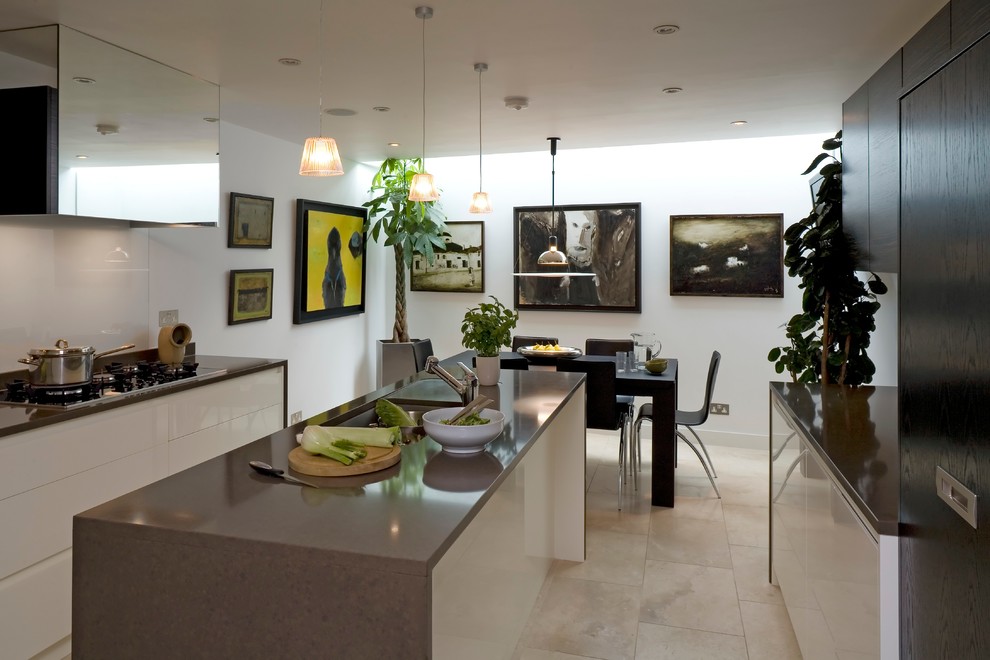 Mid-sized contemporary galley eat-in kitchen in London with a drop-in sink, flat-panel cabinets, white cabinets, solid surface benchtops, white splashback, glass sheet splashback, panelled appliances, limestone floors, with island, brown floor and brown benchtop.