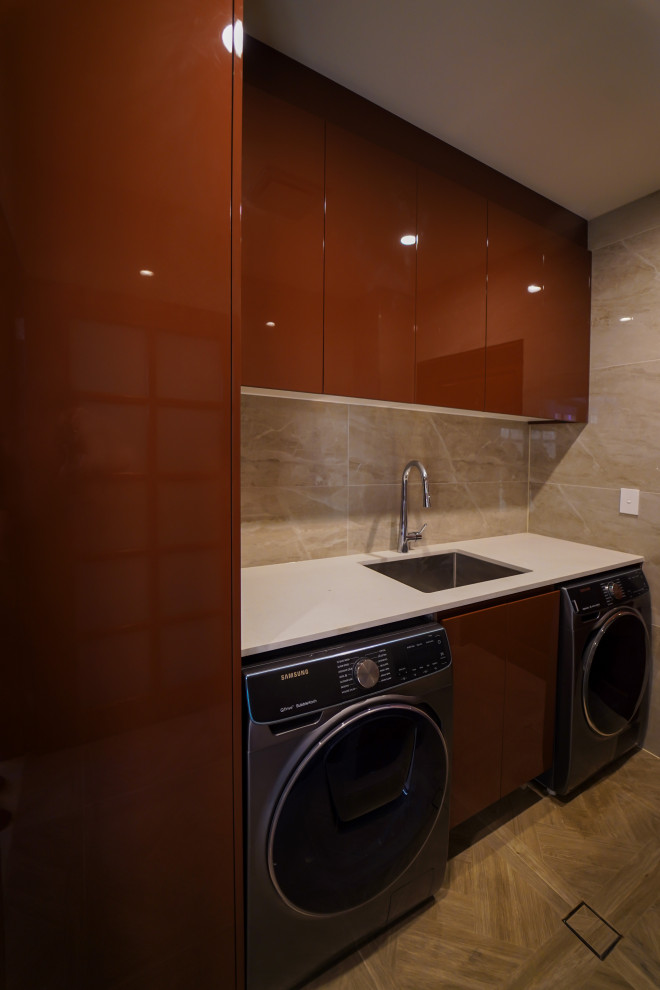 Inspiration for a mid-sized contemporary galley dedicated laundry room in Sydney with an undermount sink, flat-panel cabinets, brown cabinets, quartz benchtops, beige splashback, limestone splashback, beige walls, ceramic floors, a side-by-side washer and dryer, brown floor and white benchtop.
