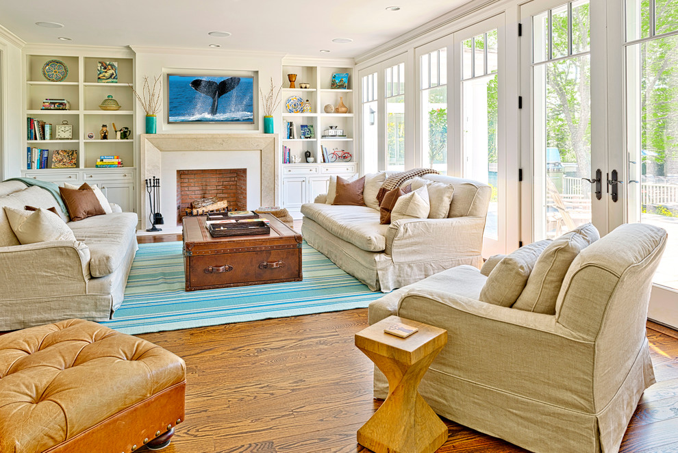This is an example of a beach style formal living room in New York with white walls, medium hardwood floors, a standard fireplace and a wall-mounted tv.