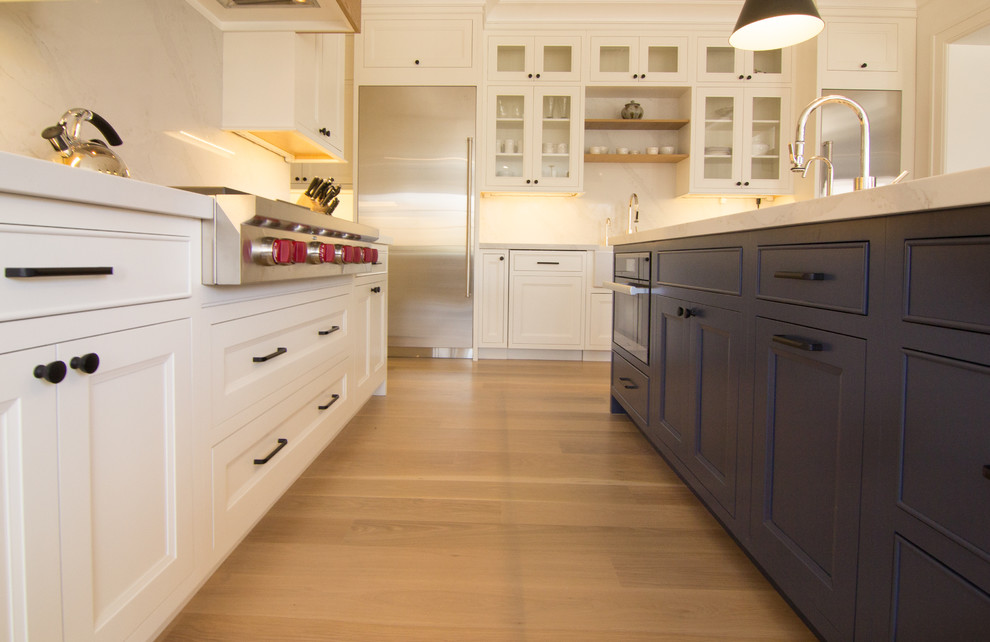 Inspiration for a large transitional u-shaped eat-in kitchen in New York with a farmhouse sink, flat-panel cabinets, white cabinets, quartzite benchtops, white splashback, stone slab splashback, stainless steel appliances, light hardwood floors, multiple islands, yellow floor and white benchtop.