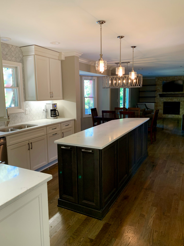 Inspiration for a mid-sized transitional l-shaped medium tone wood floor and brown floor eat-in kitchen remodel in Cincinnati with an undermount sink, flat-panel cabinets, white cabinets, quartz countertops, white backsplash, marble backsplash, stainless steel appliances, an island and white countertops