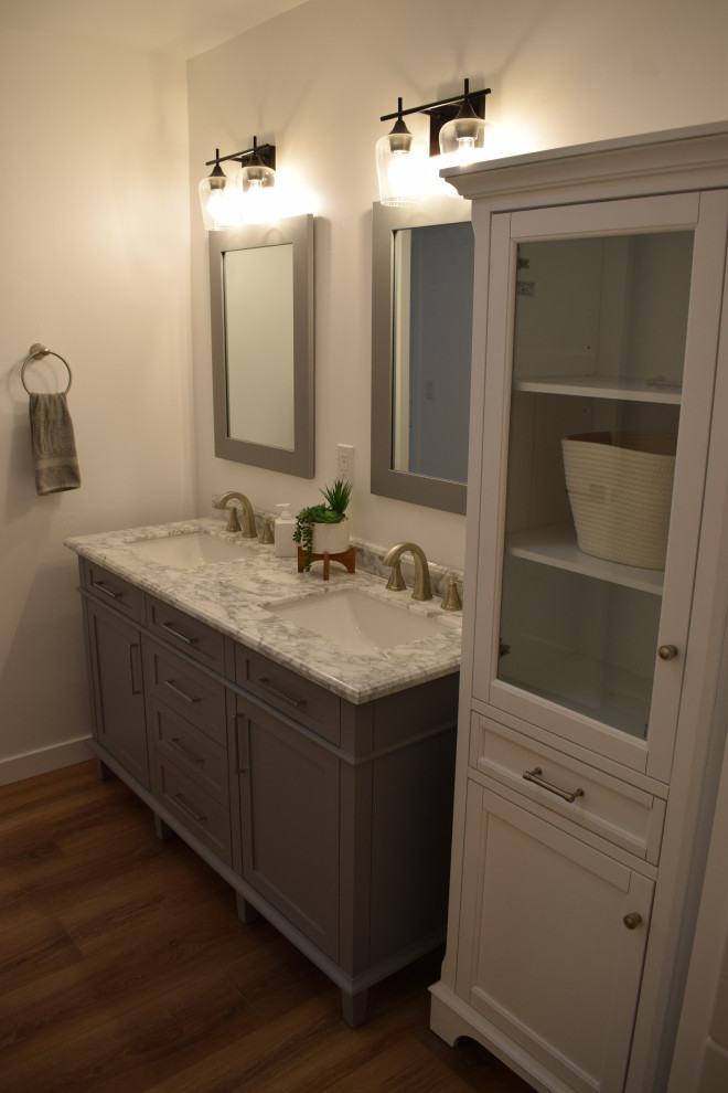 Mid-sized country master laminate floor, brown floor and double-sink bathroom photo in Santa Barbara with furniture-like cabinets, gray cabinets, a one-piece toilet, white walls, an undermount sink, quartz countertops, multicolored countertops and a freestanding vanity