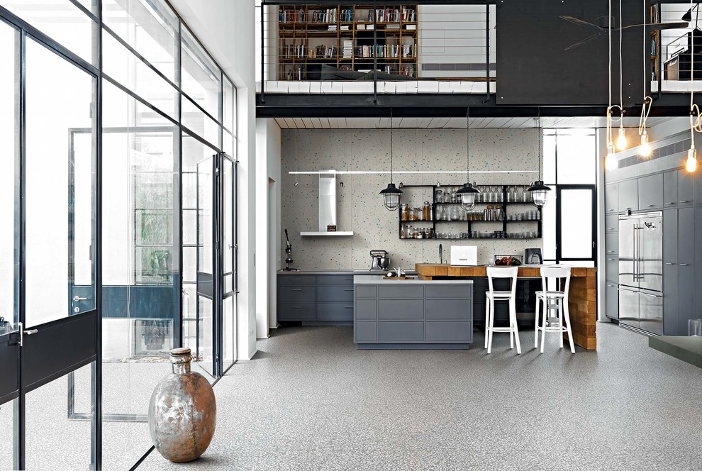 Photo of a large industrial l-shaped open plan kitchen with grey cabinets, white splashback, porcelain splashback, porcelain floors, with island, grey floor, flat-panel cabinets and stainless steel appliances.