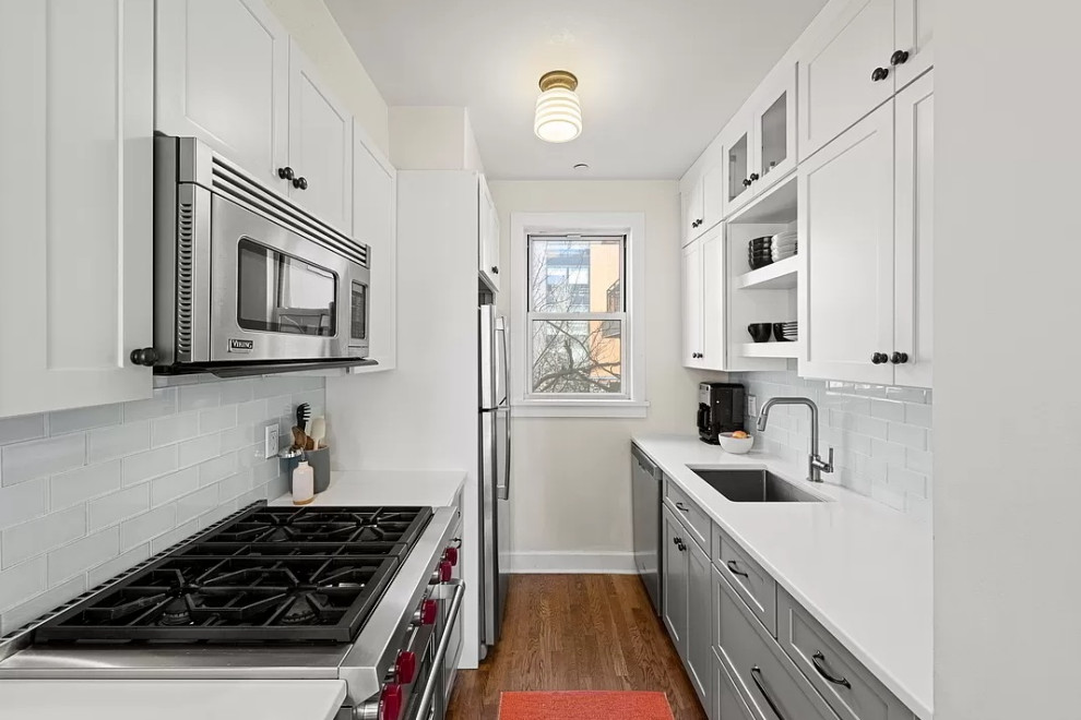 Example of a small transitional galley medium tone wood floor and brown floor enclosed kitchen design in New York with an undermount sink, shaker cabinets, white cabinets, quartz countertops, white backsplash, glass tile backsplash, stainless steel appliances, no island and white countertops