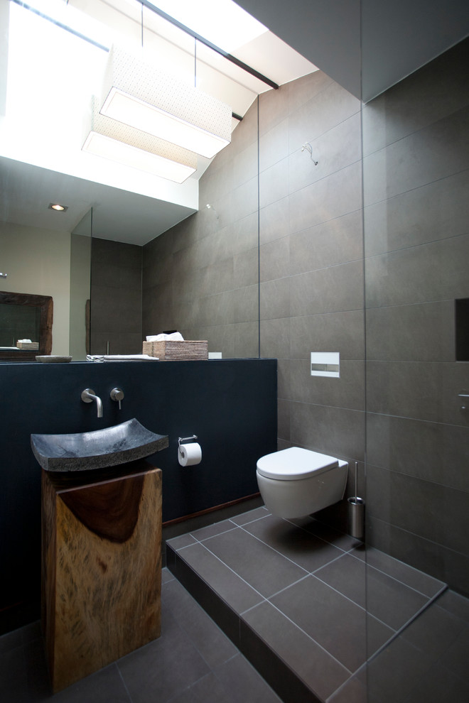 This is an example of a contemporary 3/4 bathroom in Berlin with an open shower, a wall-mount toilet, brown walls, a vessel sink, wood benchtops and an open shower.