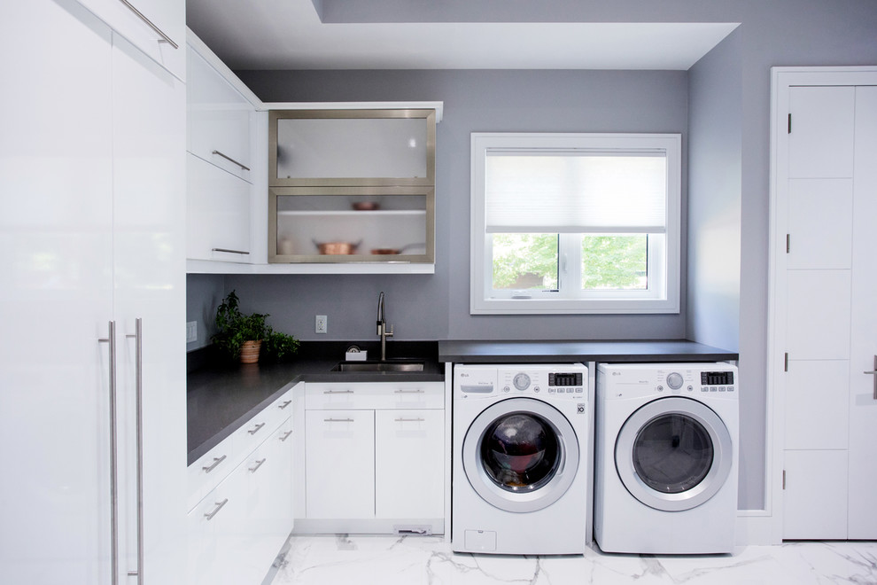 This is an example of a large modern l-shaped dedicated laundry room in Toronto with an undermount sink, flat-panel cabinets, white cabinets, quartz benchtops, grey walls, marble floors, a side-by-side washer and dryer, white floor and grey benchtop.