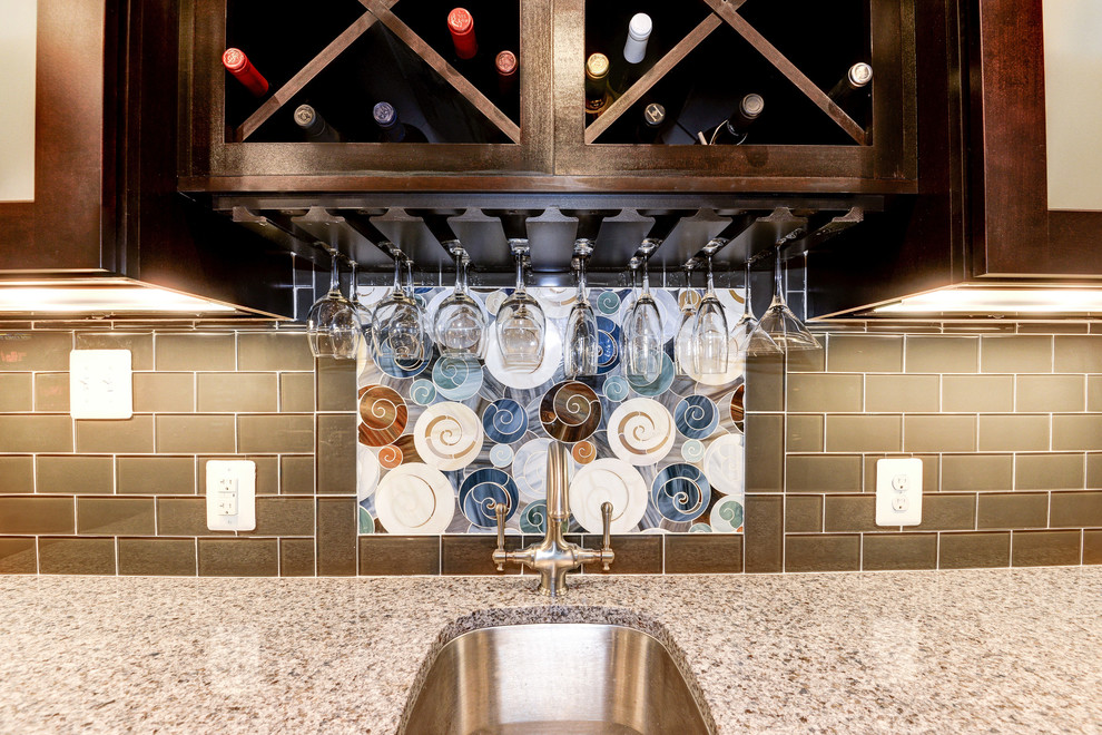 This is an example of a mid-sized traditional single-wall wet bar in DC Metro with a drop-in sink, glass-front cabinets, dark wood cabinets, granite benchtops, multi-coloured splashback, subway tile splashback and dark hardwood floors.