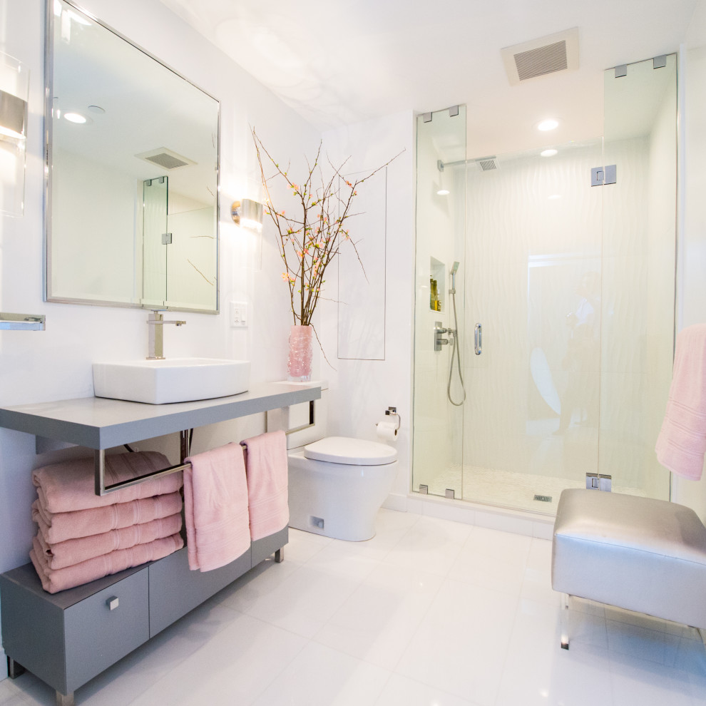 This is an example of a mid-sized contemporary master bathroom in Boston with flat-panel cabinets, grey cabinets, an alcove shower, a one-piece toilet, white tile, ceramic tile, white walls, ceramic floors, a vessel sink, solid surface benchtops, white floor, an open shower and grey benchtops.