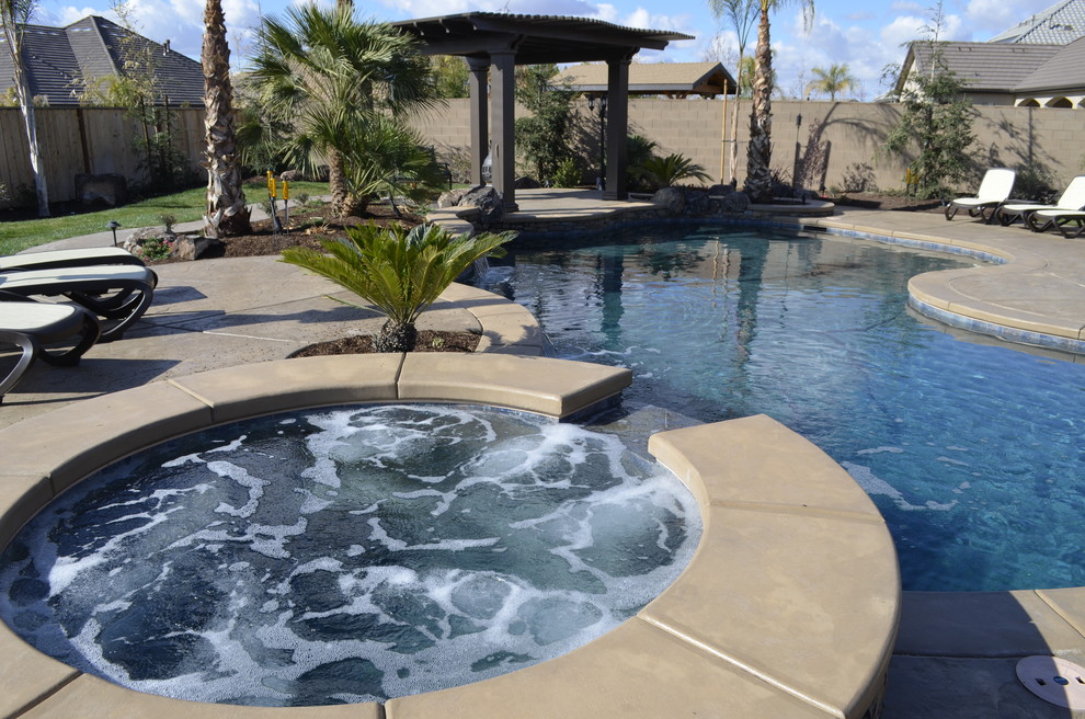 Photo of a large tropical backyard custom-shaped natural pool in Other with stamped concrete and a hot tub.