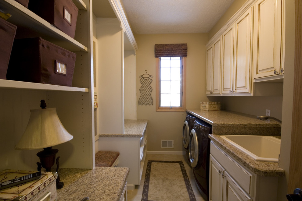 Photo of a mid-sized traditional galley dedicated laundry room in Other with a drop-in sink, raised-panel cabinets, distressed cabinets, beige walls, ceramic floors and a side-by-side washer and dryer.