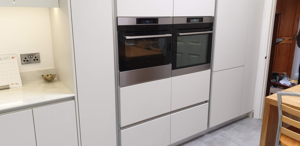 This is an example of a large modern u-shaped eat-in kitchen in Other with an undermount sink, flat-panel cabinets, white cabinets, onyx benchtops, white splashback, black appliances, linoleum floors, with island, grey floor and white benchtop.