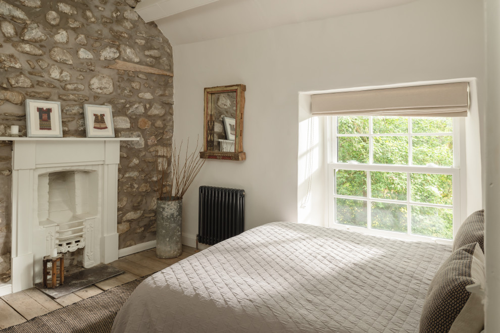 Photo of a country guest bedroom in Other with white walls, light hardwood floors, a standard fireplace, a brick fireplace surround and exposed beam.