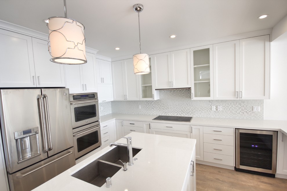 Photo of a large transitional u-shaped eat-in kitchen in Los Angeles with a double-bowl sink, shaker cabinets, white cabinets, marble benchtops, grey splashback, mosaic tile splashback, stainless steel appliances, light hardwood floors and with island.