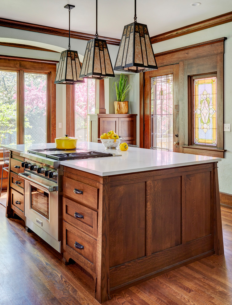 This is an example of a mid-sized arts and crafts kitchen in Milwaukee with a farmhouse sink, shaker cabinets, medium wood cabinets, quartz benchtops, white splashback, subway tile splashback, stainless steel appliances, medium hardwood floors, with island, brown floor and white benchtop.