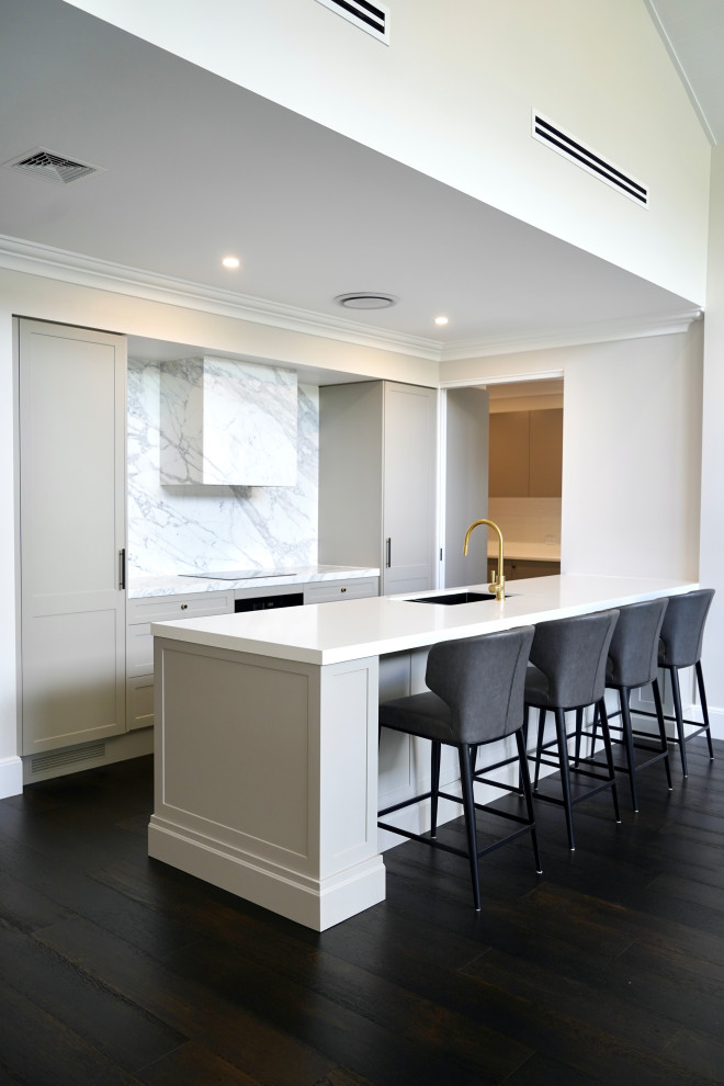 Inspiration for a large transitional single-wall open plan kitchen in Sydney with an undermount sink, shaker cabinets, grey cabinets, marble benchtops, white splashback, marble splashback, black appliances, dark hardwood floors, with island, brown floor and white benchtop.