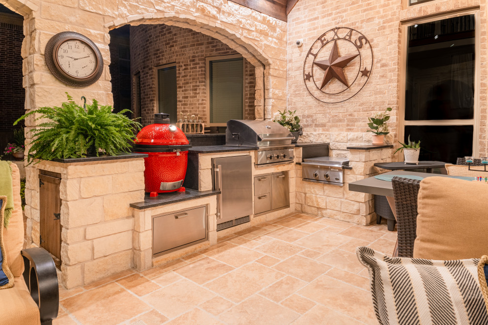 This is an example of a mid-sized transitional backyard patio in Dallas with an outdoor kitchen, natural stone pavers and a roof extension.