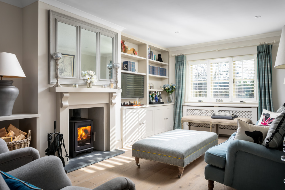 This is an example of a large transitional formal enclosed living room in Gloucestershire with white walls, a wood stove, light hardwood floors, a built-in media wall and beige floor.