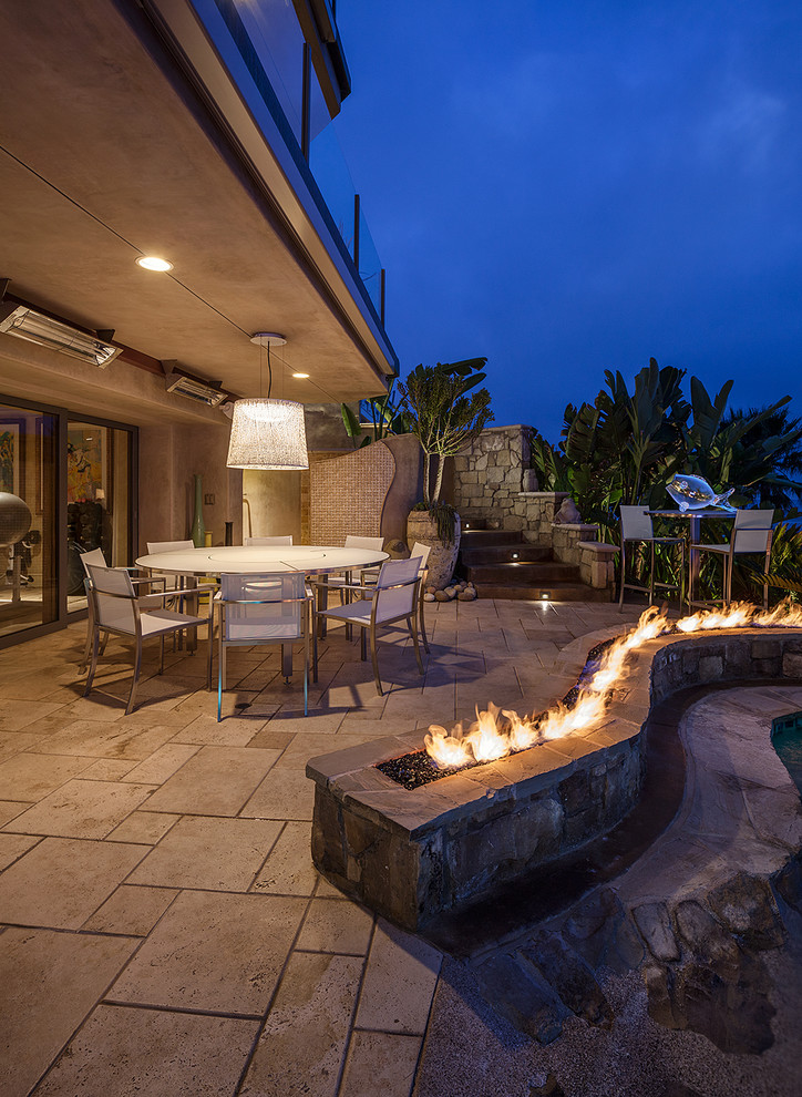 Photo of a large tropical backyard patio in Los Angeles with a fire feature, a roof extension and concrete pavers.