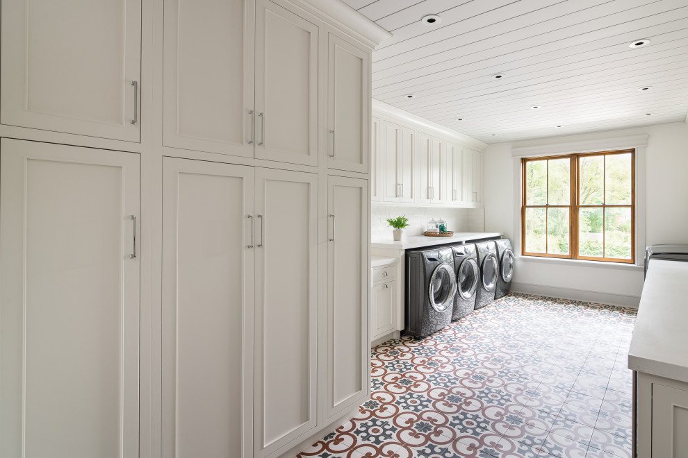 This is an example of an expansive country laundry room in New York with a farmhouse sink, beaded inset cabinets, white cabinets, quartz benchtops, white splashback, subway tile splashback, white walls, ceramic floors, a side-by-side washer and dryer, blue floor, white benchtop, timber and planked wall panelling.