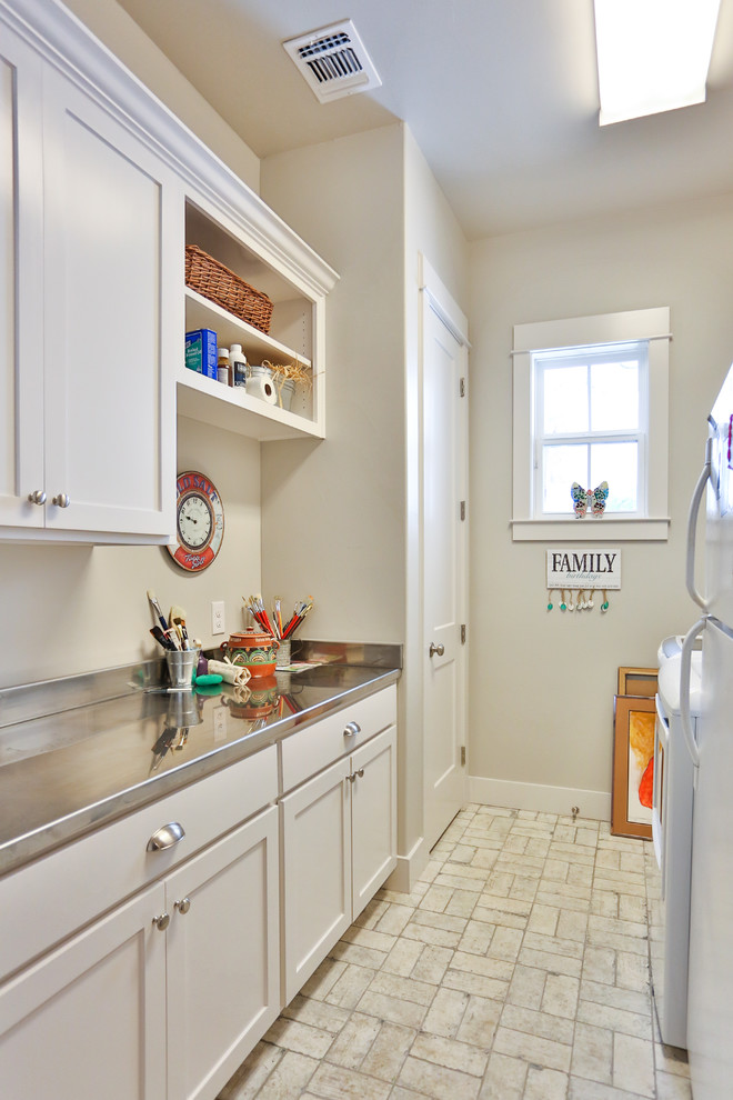 Small traditional galley dedicated laundry room in Austin with recessed-panel cabinets, white cabinets, stainless steel benchtops, beige walls, a side-by-side washer and dryer and grey benchtop.