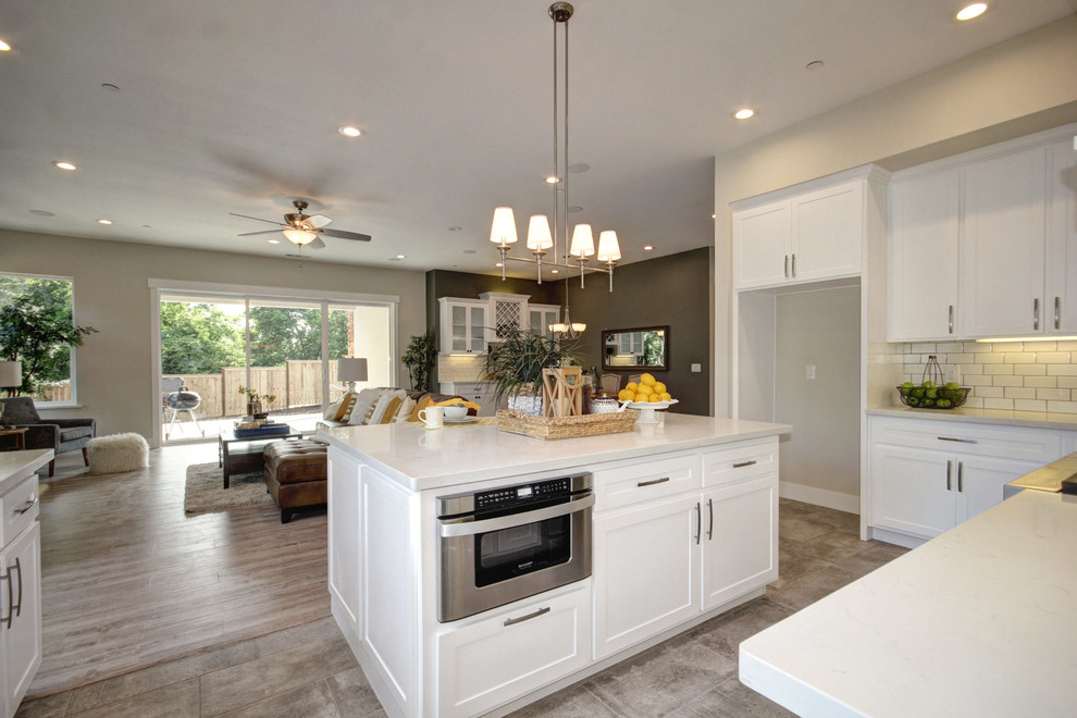 Inspiration for a mid-sized traditional u-shaped open plan kitchen in Sacramento with a farmhouse sink, shaker cabinets, white cabinets, quartzite benchtops, white splashback, subway tile splashback, stainless steel appliances, ceramic floors, with island, grey floor and white benchtop.