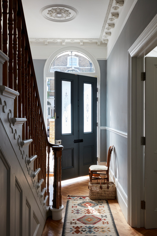 Réalisation d'une grande porte d'entrée victorienne avec un mur gris, un sol en bois brun, une porte simple et une porte grise.