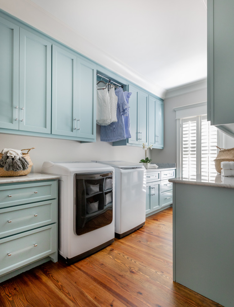 Photo of a large transitional galley dedicated laundry room in Atlanta with shaker cabinets, blue cabinets, quartz benchtops, beige walls, medium hardwood floors, a side-by-side washer and dryer, brown floor and grey benchtop.