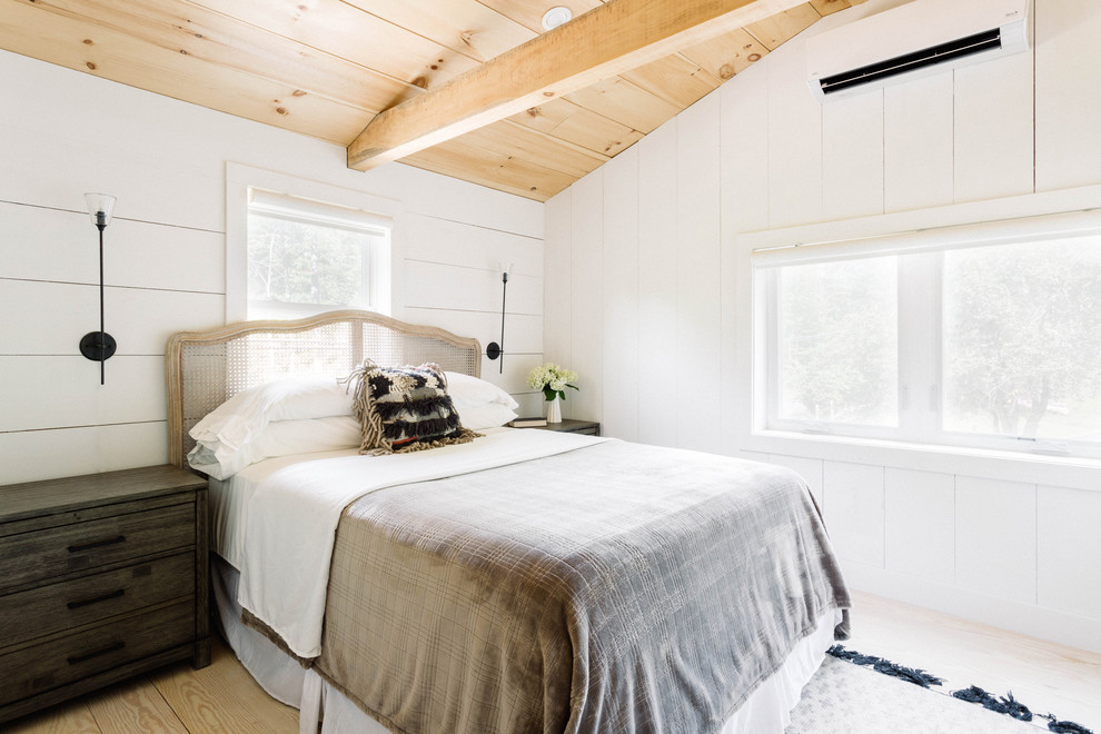 Photo of a small country guest bedroom in New York with white walls, light hardwood floors, a wood stove and white floor.