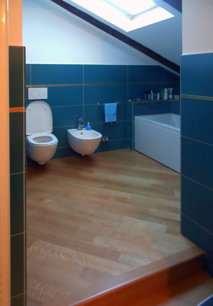 Cette image montre une grande salle de bain principale minimaliste avec un carrelage bleu, un mur blanc, WC suspendus, un sol marron, poutres apparentes, une baignoire en alcôve, des carreaux de porcelaine, parquet clair, un lavabo encastré, un plan de toilette en marbre, un plan de toilette blanc, meuble simple vasque et meuble-lavabo sur pied.