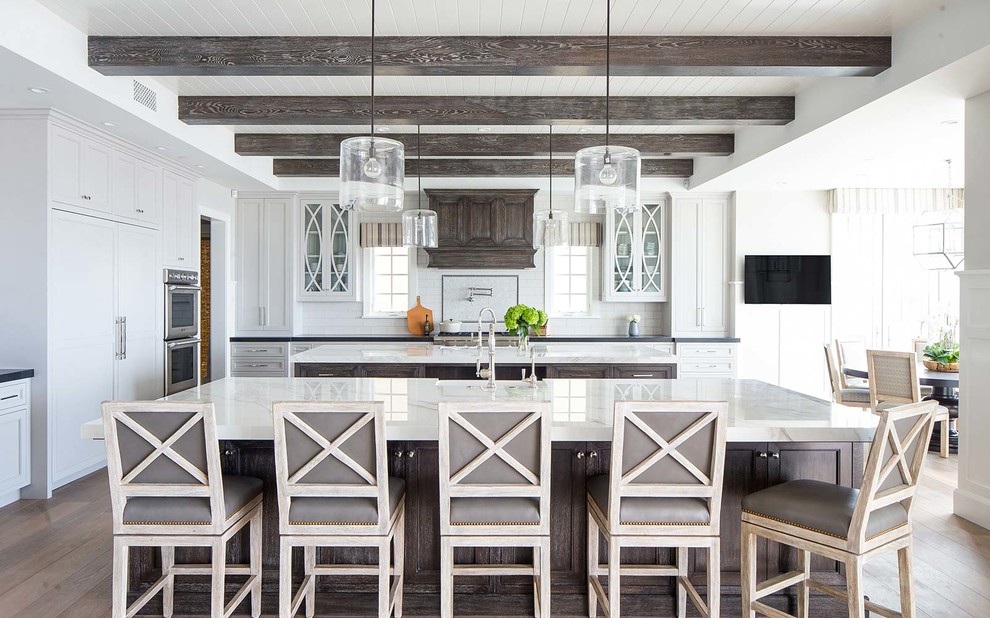 Inspiration for a beach style eat-in kitchen in Other with a farmhouse sink, grey cabinets, white splashback, subway tile splashback, stainless steel appliances, dark hardwood floors, multiple islands, brown floor, black benchtop and recessed-panel cabinets.
