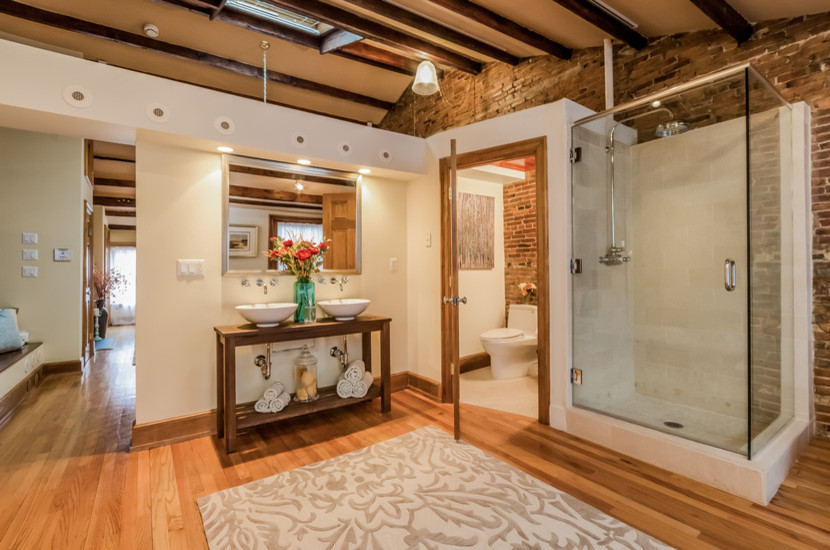 This is an example of a large industrial master bathroom in Boston with open cabinets, dark wood cabinets, a claw-foot tub, a corner shower, a one-piece toilet, beige tile, travertine, white walls, dark hardwood floors, a vessel sink, wood benchtops, brown floor and a hinged shower door.