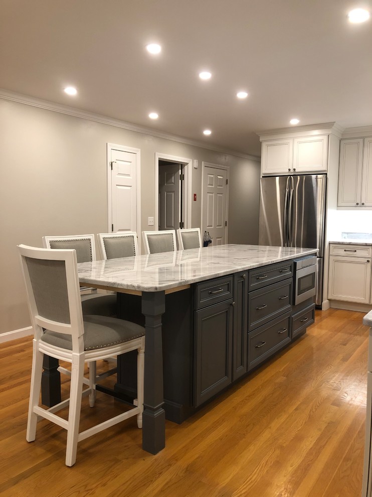 Large transitional l-shaped open plan kitchen in Boston with an undermount sink, recessed-panel cabinets, white cabinets, quartz benchtops, white splashback, subway tile splashback, stainless steel appliances, medium hardwood floors, with island, brown floor and multi-coloured benchtop.